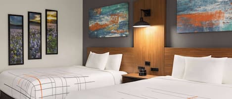 A hotel room with two beds, a wooden headboard, a nightstand, and three framed pictures on the wall.