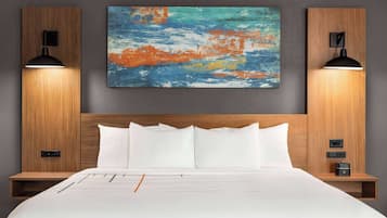 Una habitación de hotel con una cama grande, dos mesitas de noche, una lámpara de noche, un cuadro colgado en la pared y dos lámparas de pared.