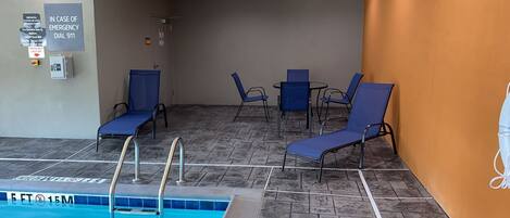 A pool area with lounge chairs, a pool ladder, and emergency information signs.