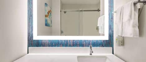 A bathroom with a white sink, a large mirror, and a shower visible in the reflection.
