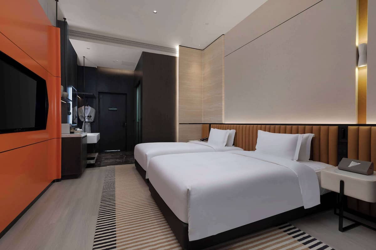 Ein Hotelzimmer mit zwei Betten, einem Fernseher, einem Schreibtisch und einem Badezimmer.