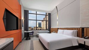 Une chambre d’hôtel moderne dotée d’un grand lit, d’une télévision à écran plat, d’une petite table et offrant une vue sur le paysage urbain.