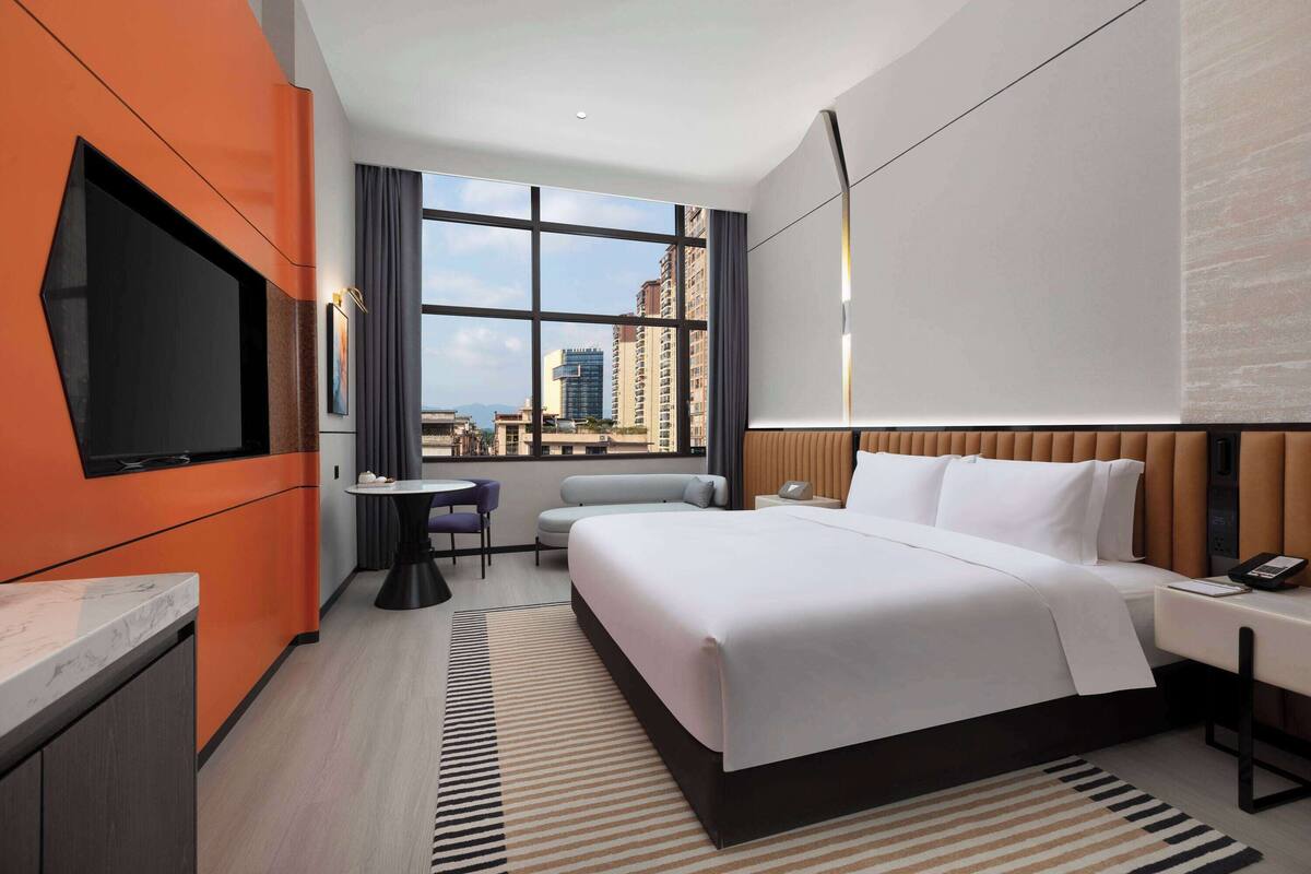 Ein modernes Hotelzimmer mit einem großen Bett, einem Flachbildfernseher, einem kleinen Tisch und Blick auf die Stadt.