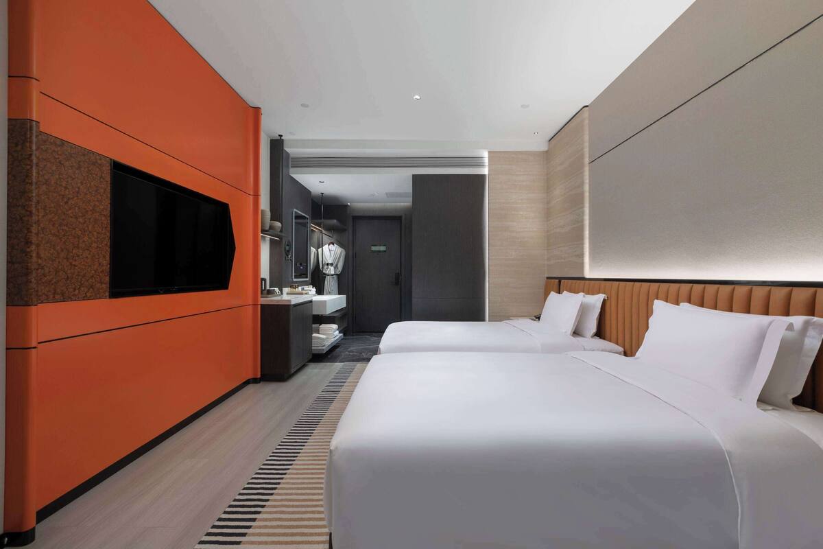 Ein modernes Hotelzimmer mit zwei Betten, einem Fernseher, einem Badezimmer und Blick auf den Flur.