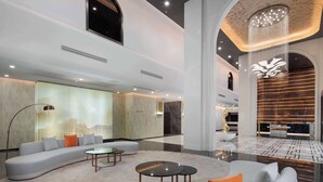Un hall d’entrée spacieux, avec un canapé incurvé, des tables rondes et un lustre.