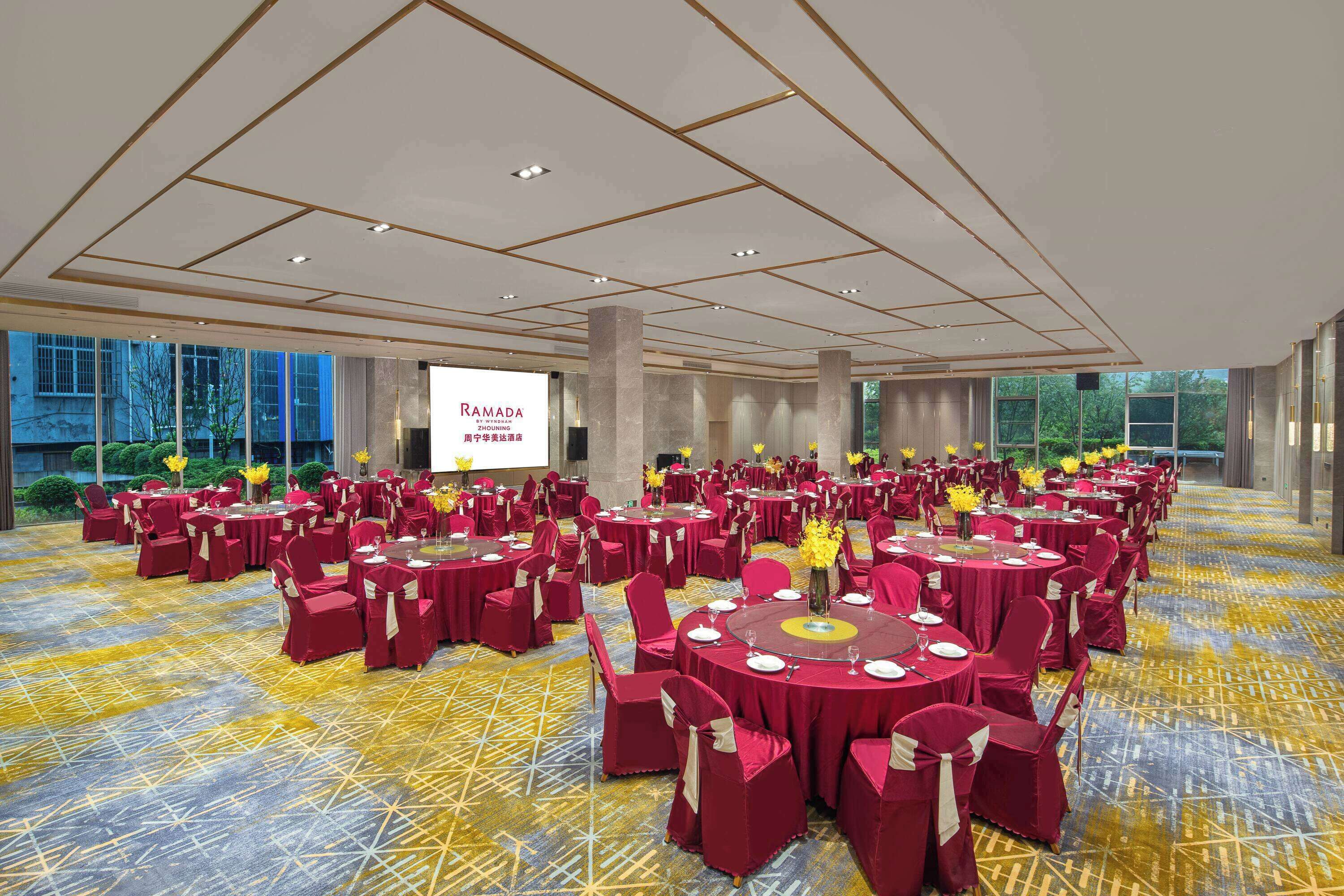 A large banquet hall with round tables and chairs, a projector screen, and a patterned carpet.