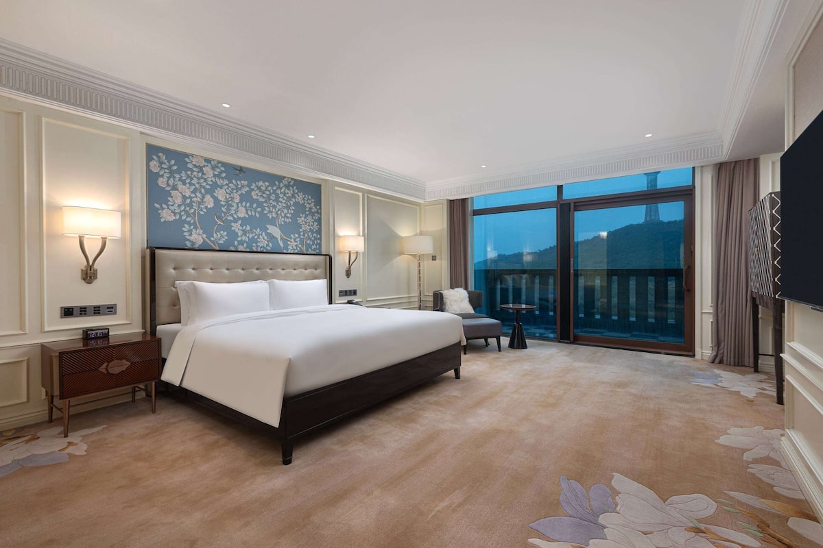 Une chambre d’hôtel spacieuse, dotée d’un grand lit, d’un coin salon et d’un balcon offrant une vue sur la ville.