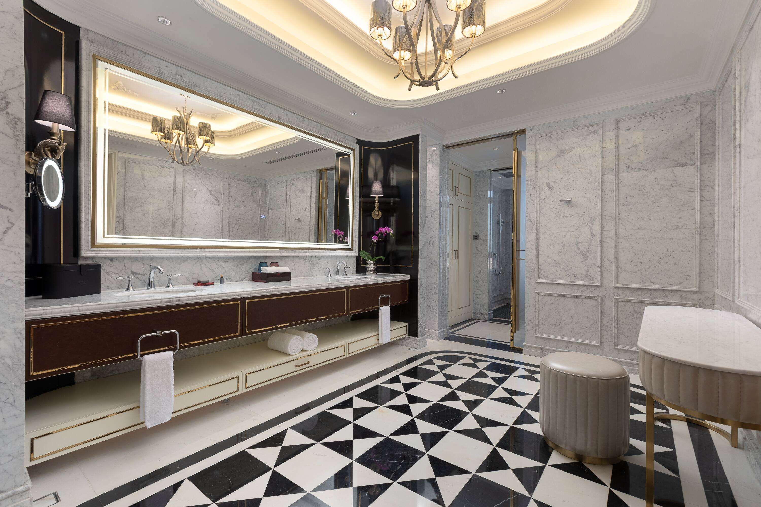 A modern bathroom with a large mirror, dual sinks, a round vanity, and a black and white checkered floor.