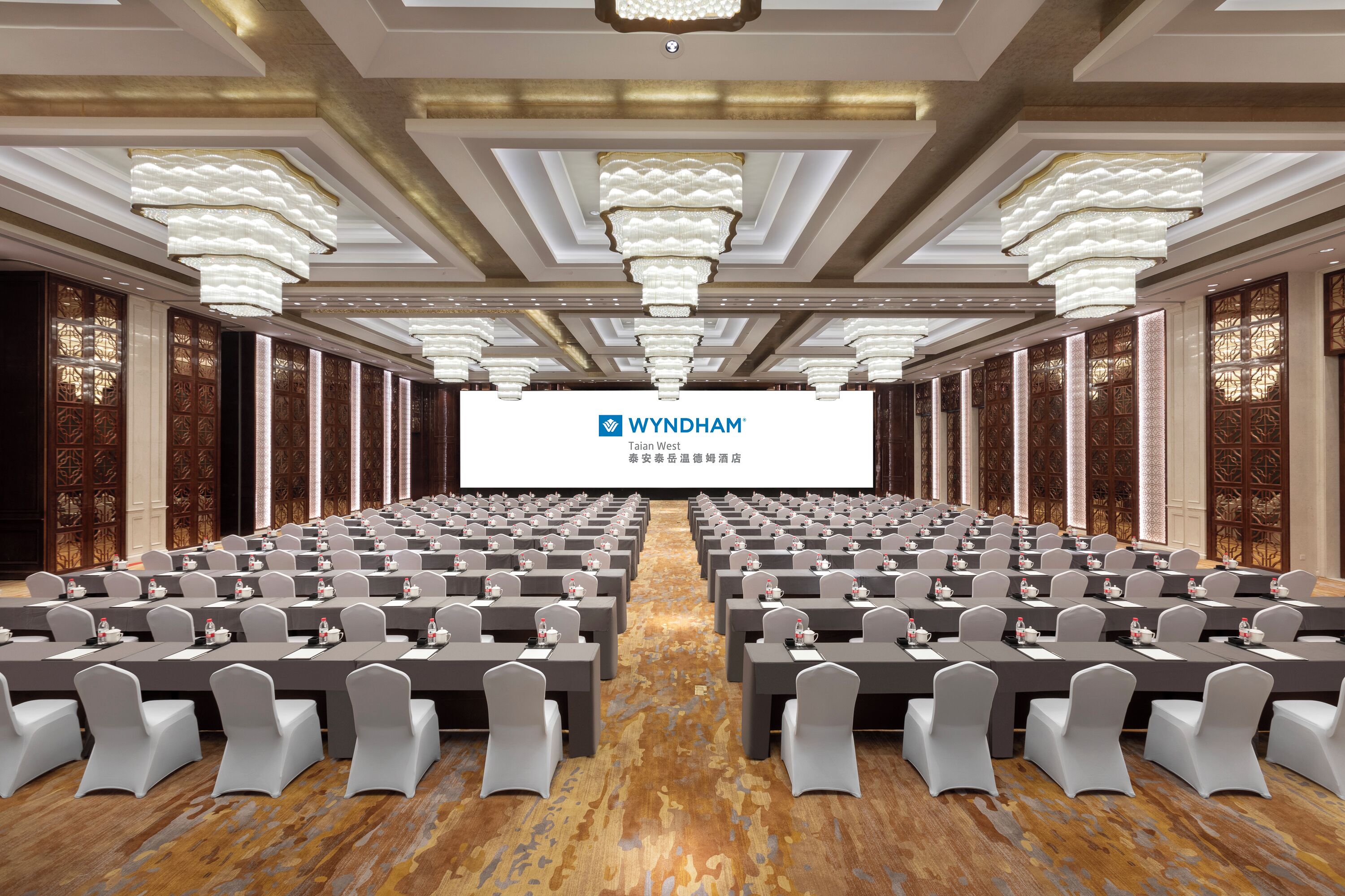Un salón de conferencias con filas de mesas y sillas, una pantalla grande al frente y elaboradas decoraciones en el techo.