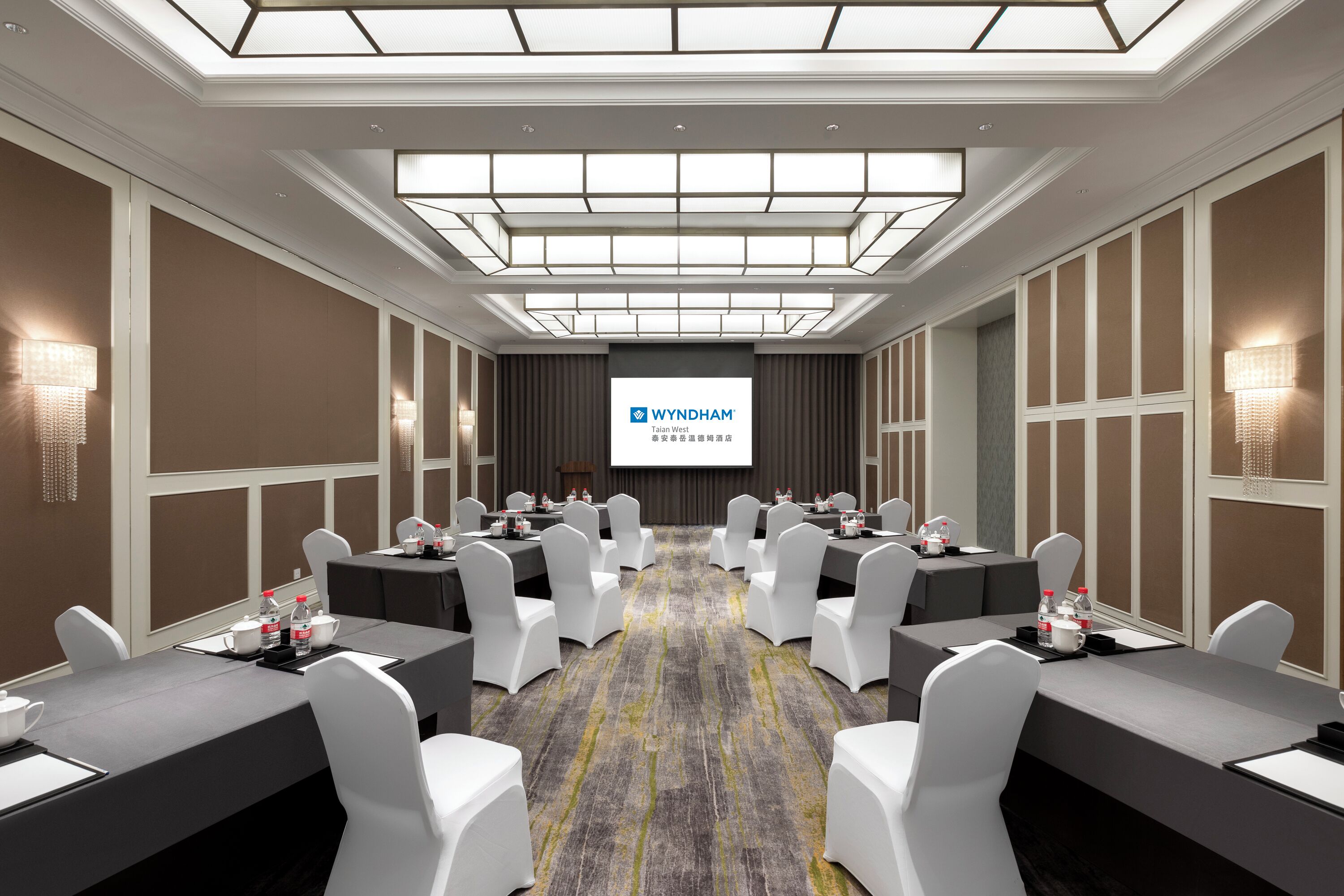 A conference room with a large screen displaying 'WYNDHAM' branding, multiple tables with chairs, and a patterned carpet.