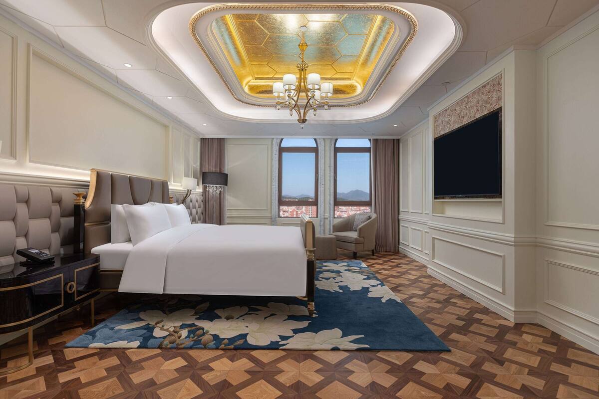 Une chambre d’hôtel luxueuse, dotée d’un grand lit, d’un lustre, d’une télévision à écran plat et offrant une vue sur la ville.