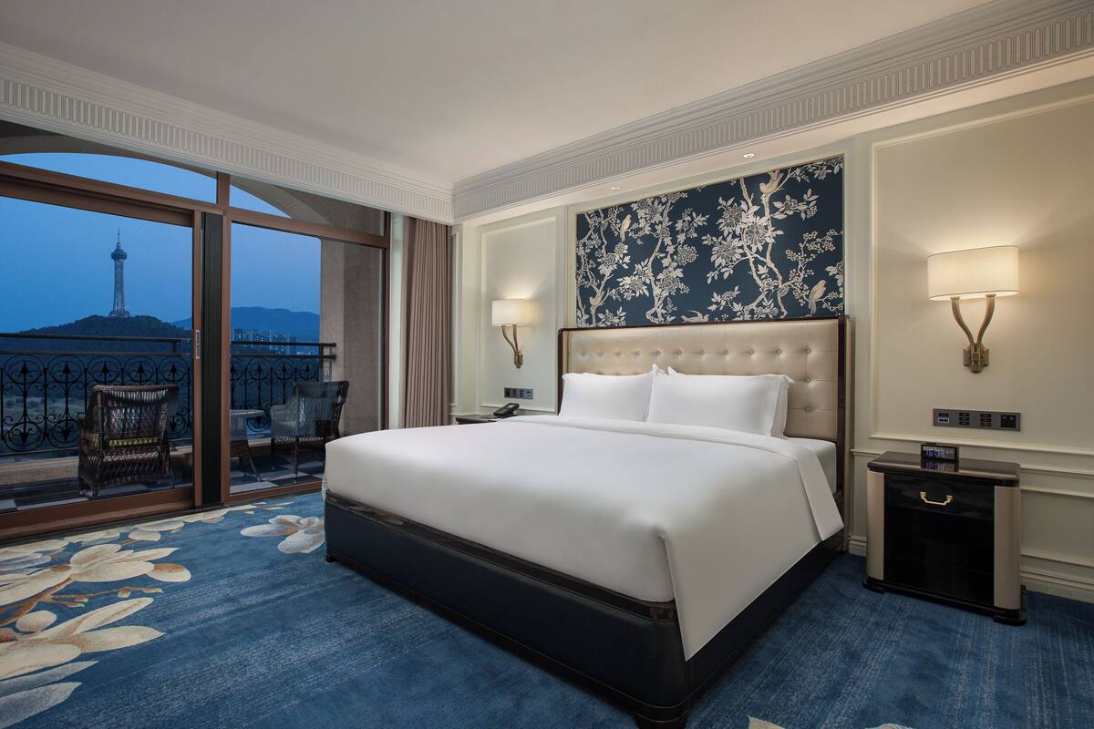 Une chambre d’hôtel avec un grand lit, deux lampes de chevet, une table de chevet, une vue sur la tour et un balcon avec des chaises.