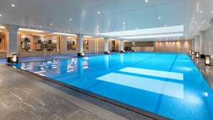 Un'ampia piscina interna con acqua cristallina e limpida, circondata da pavimenti in marmo e moderne lampade.