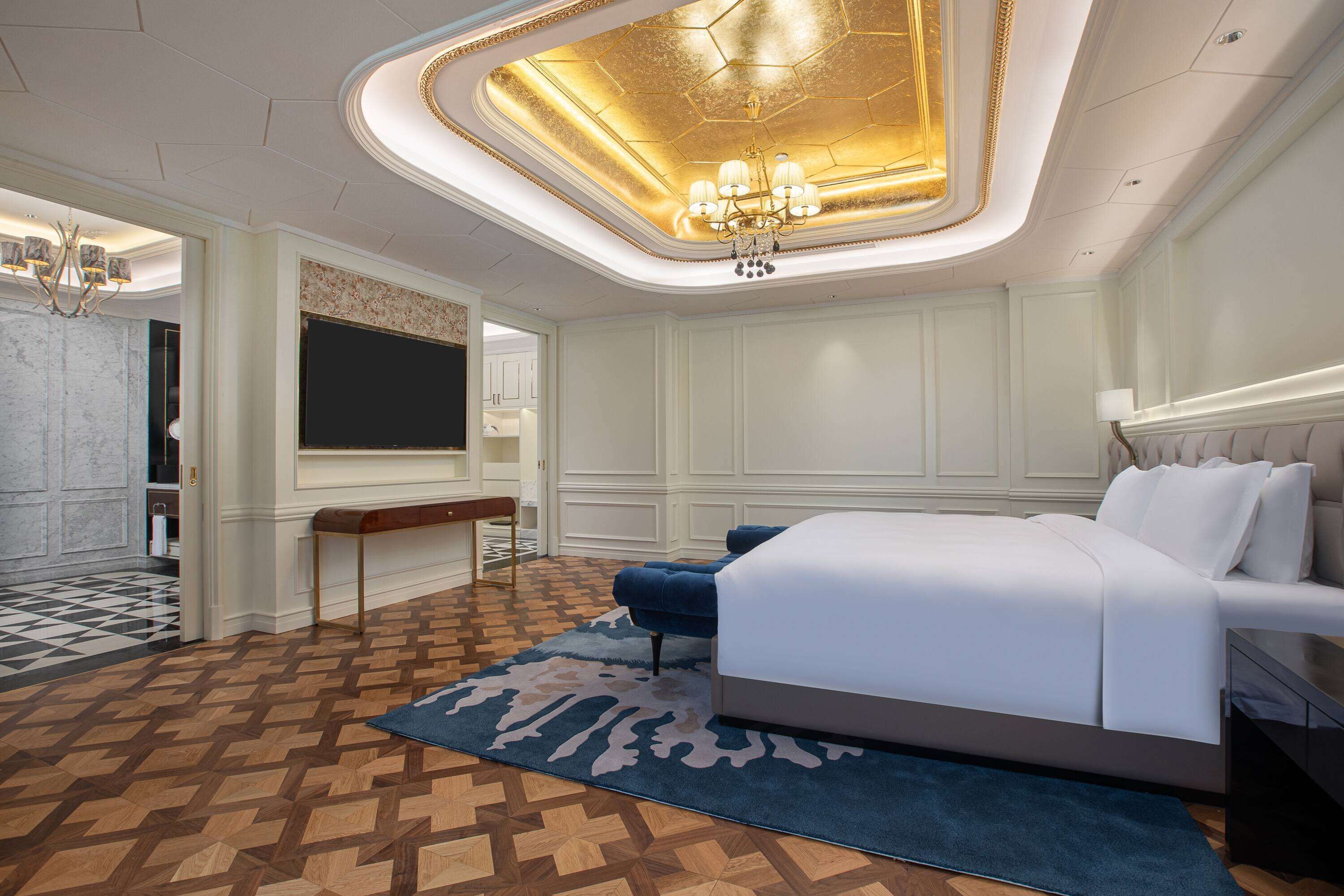 A modern bedroom with a large bed, a desk, and a chandelier.