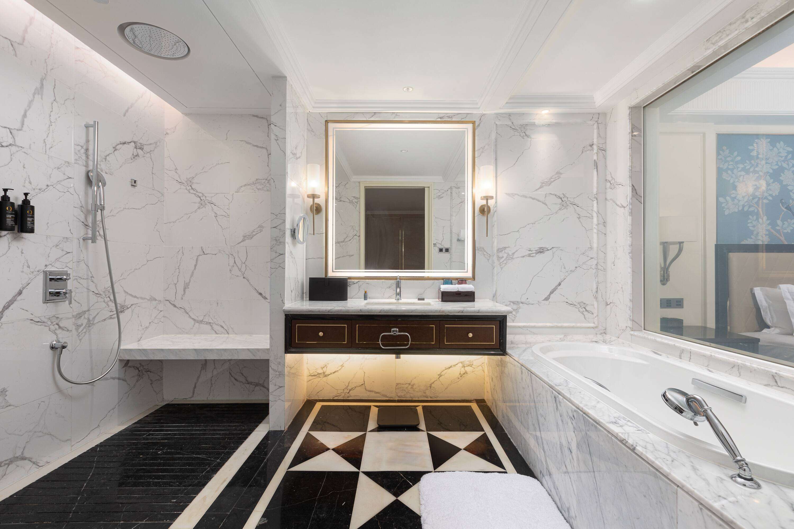Un baño moderno con piso de mármol, un espejo grande, una bañera y una zona de ducha.
