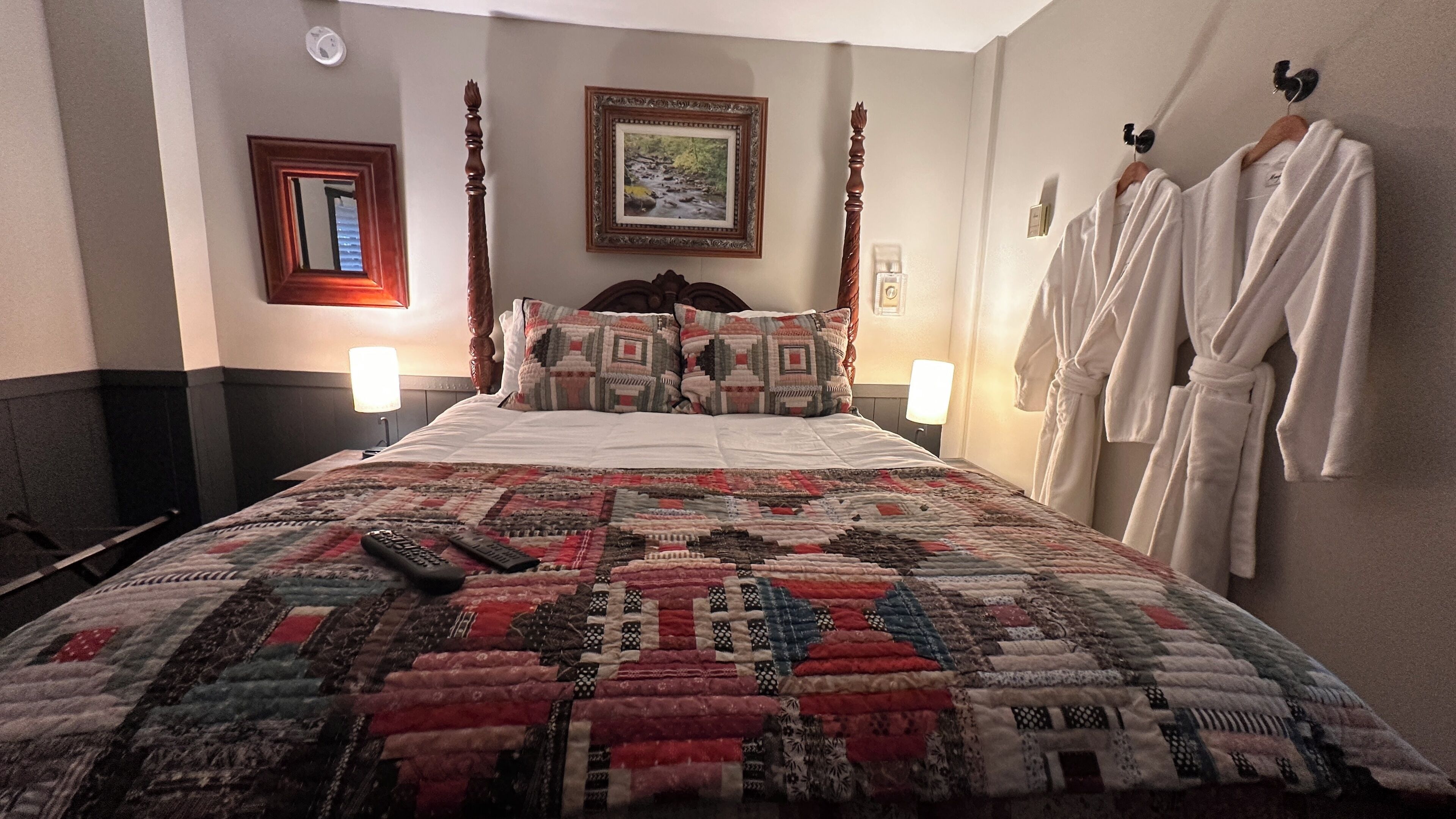 A neatly made bed with a patterned quilt, two bedside lamps, a framed picture on the wall, and a wooden headboard.