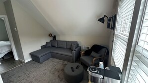 Una sala de estar moderna con un sofá seccional gris, un otomano redondo pequeño, un sillón negro y una mesa de centro.