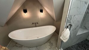 Un baño moderno con una bañera independiente, paredes cubiertas de mármol y dos luces fijadas a la pared.