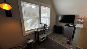 Un espacio habitable compacto con kitchenette, televisor, cafetera y extintor.