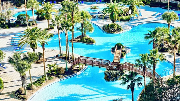 A resort with multiple swimming pools, palm trees, and a wooden bridge. - 1509 Stunning 2 Bdrm ~ Lagoon Pool ~ Pickleball - Gym - Hot tub ~ Book Sept 8th (Destin)