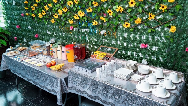 A buffet table with various food items and utensils, set against a backdrop of artificial flowers and greenery. - HOTEL TERRANORT (Iquique)