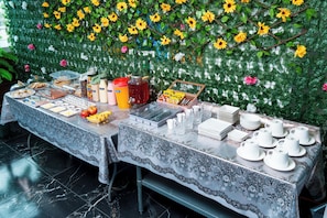 A buffet table with various food items and utensils, set against a backdrop of artificial flowers and greenery. - HOTEL TERRANORT (Iquique)