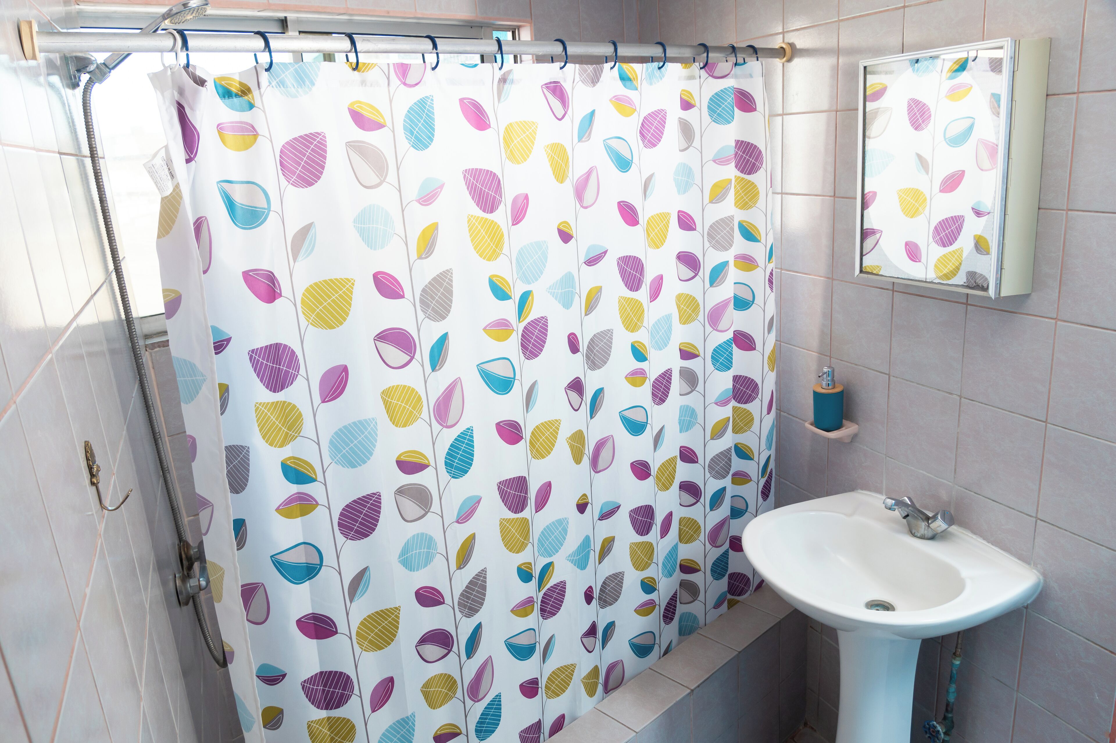 Un baño con cortina de ducha estampada con hojas, un lavabo blanco y un espejo sobre él.