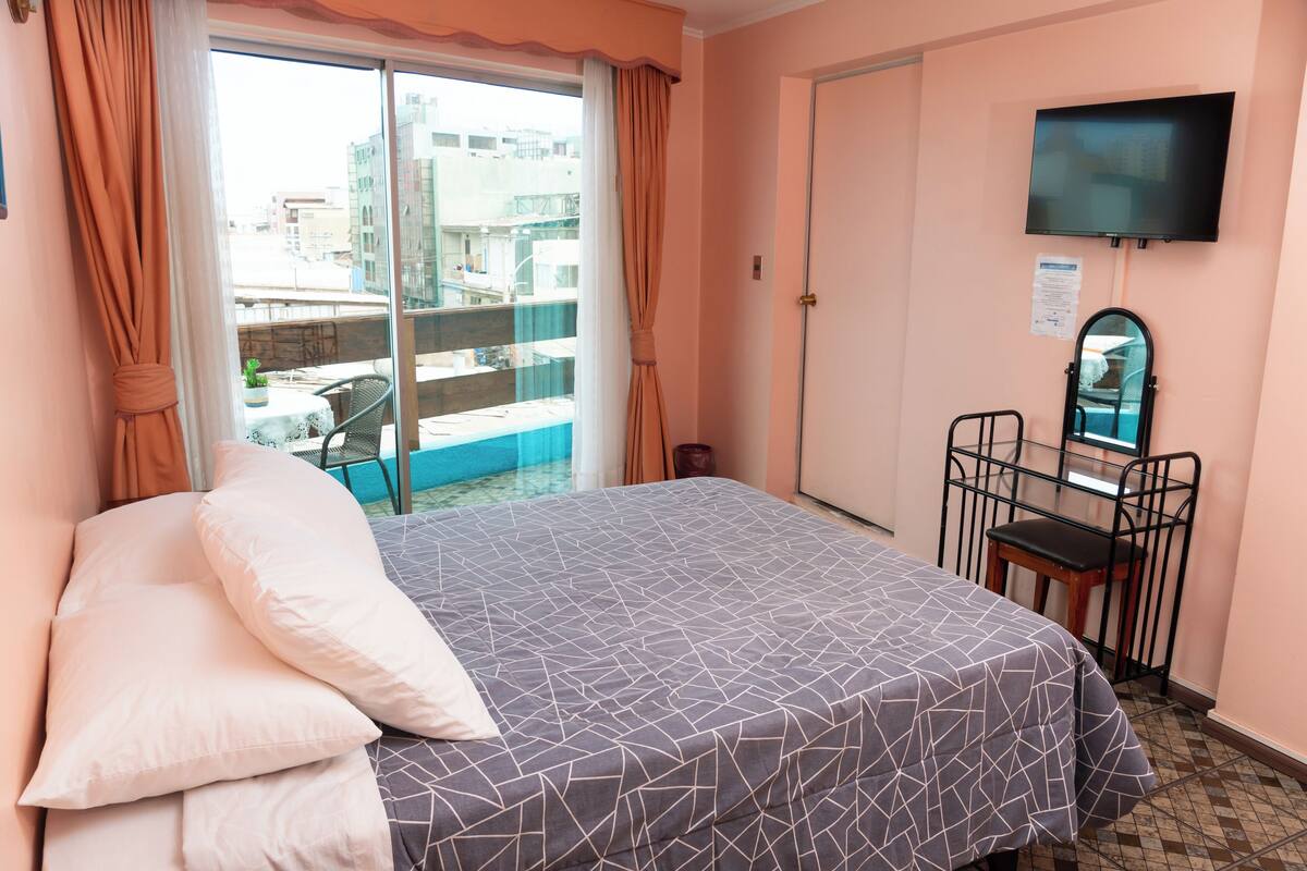 Une chambre d’hôtel équipée d’un lit, d’une télévision, d’une chaise et d’un balcon avec vue sur les bâtiments.