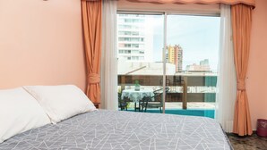 A hotel room with a bed, a balcony with a table and chairs, and a view of the cityscape. - HOTEL TERRANORT (Iquique)