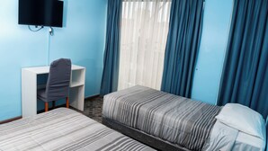 A hotel room with two single beds, a desk, a chair, a TV mounted on the wall, and a window with curtains. - HOTEL TERRANORT (Iquique)