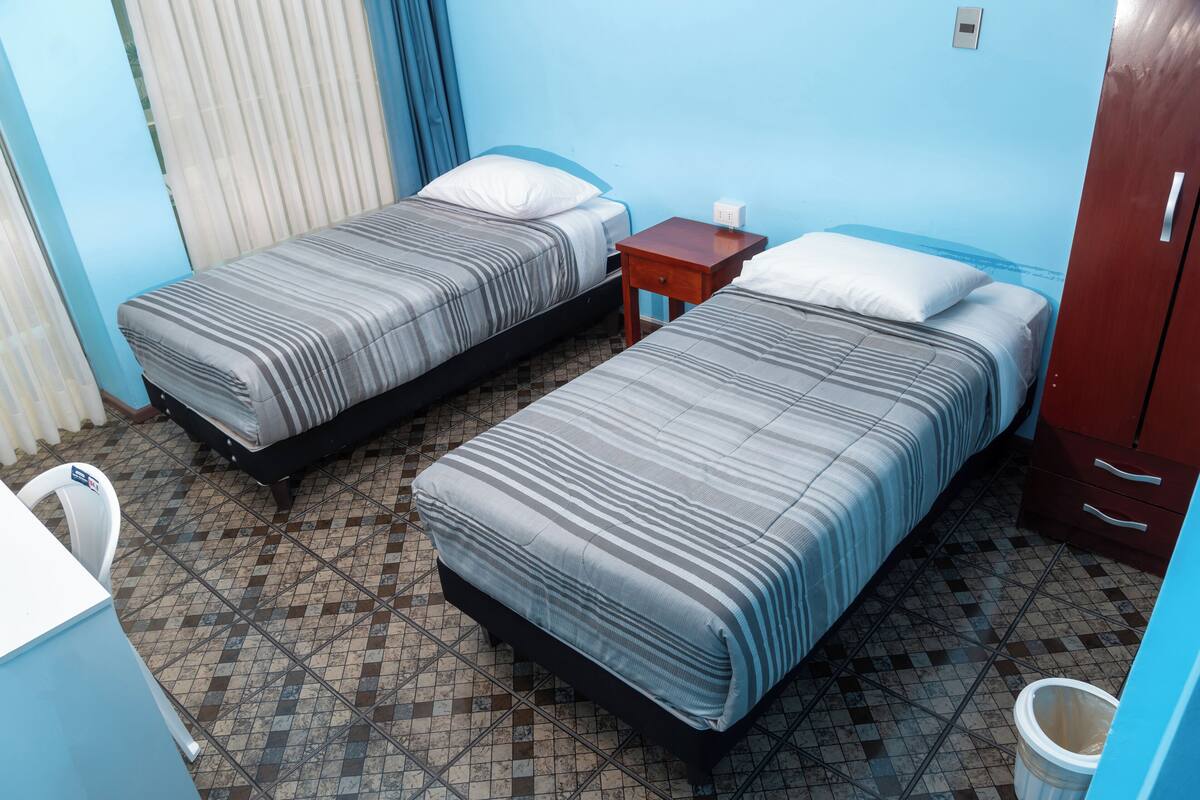 Une chambre avec deux lits, une petite table, une chaise et un placard.