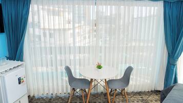 A room with a white table, two grey chairs, a small plant on the table, and a refrigerator on the left.