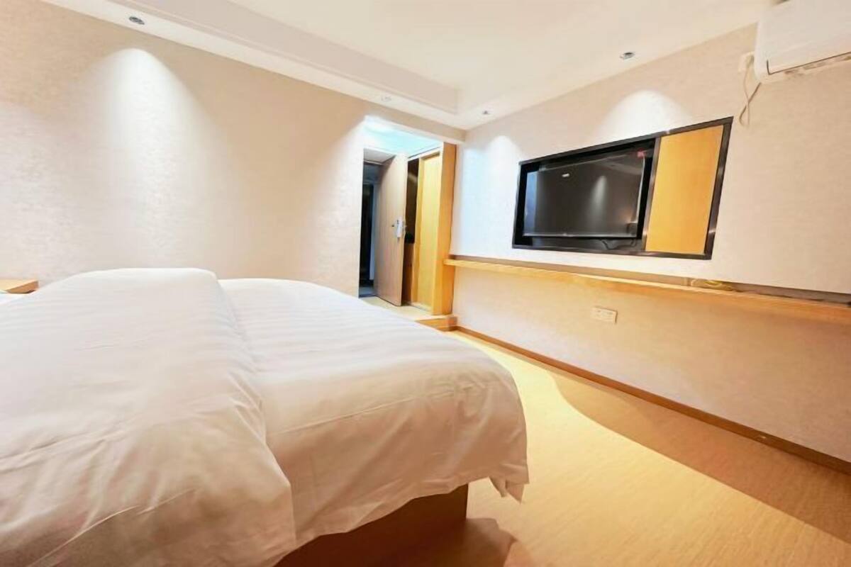 Ein Hotelzimmer mit Bett, einem an der Wand montierten Fernseher und einer Tür zu einem weiteren Raum.