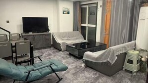 A modern living room with a sofa, a recliner, a glass coffee table, and a television. - Kuaile Holiday Hotel (Lianyungang)