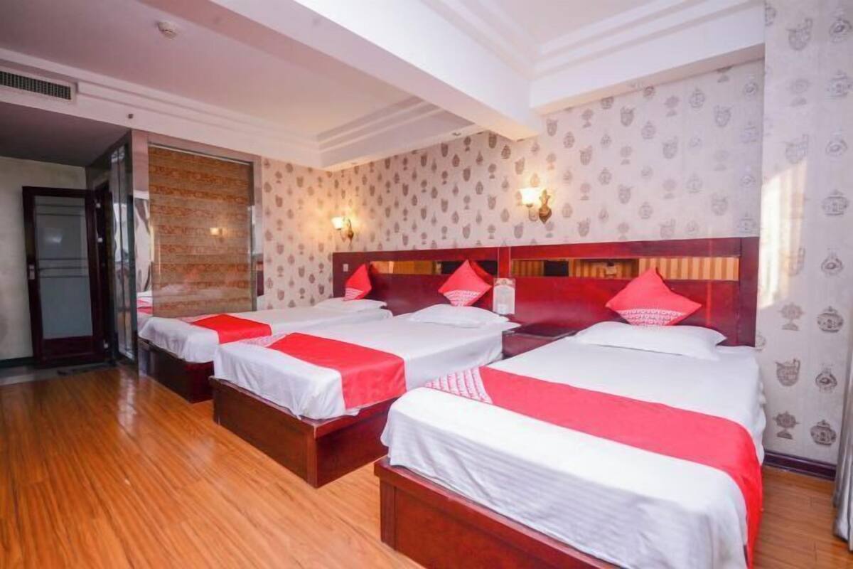 Ein Hotelzimmer mit drei Betten, jeweils mit roter und weißer Bettwäsche, Holz-Kopfteilen und Wandpapier mit Muster.