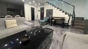 A modern living room with a sofa, a coffee table, and a staircase. - Kuaile Holiday Hotel (Lianyungang)