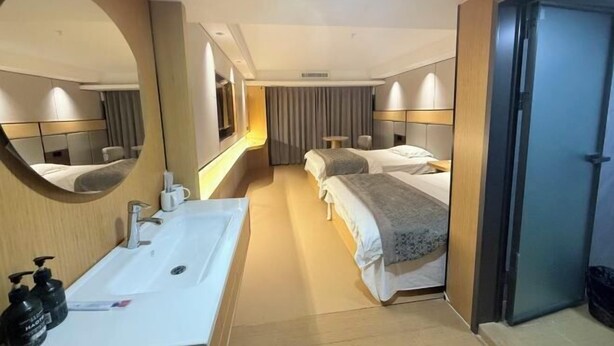 A hotel room with a large mirror, a sink, two beds, and a door. - Kuaile Holiday Hotel (Lianyungang)