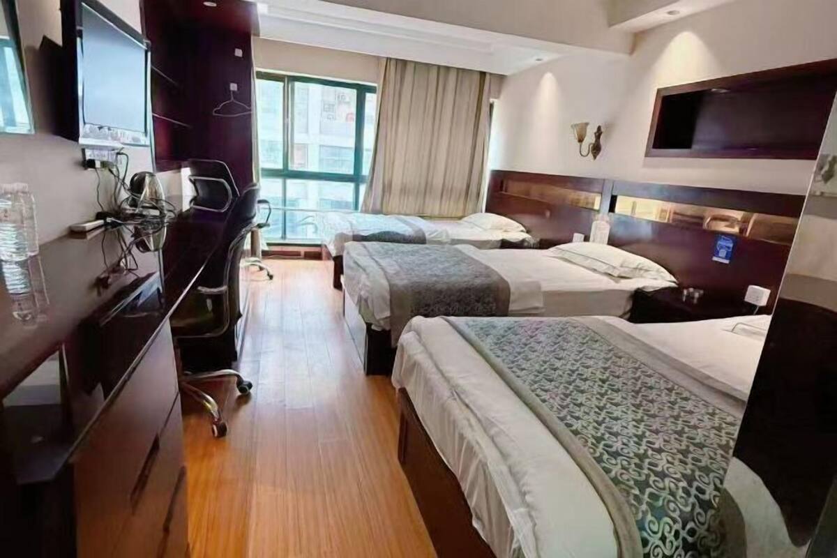 Ein Hotelzimmer mit zwei Betten, einem Schreibtisch mit Stuhl, einem Fernseher und einem Fenster mit Vorhängen.