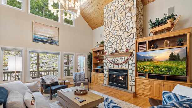 A spacious living room with a stone fireplace, large windows, and a cozy seating area.