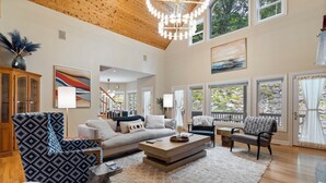 A spacious living room with a high ceiling, large windows, and a fireplace.