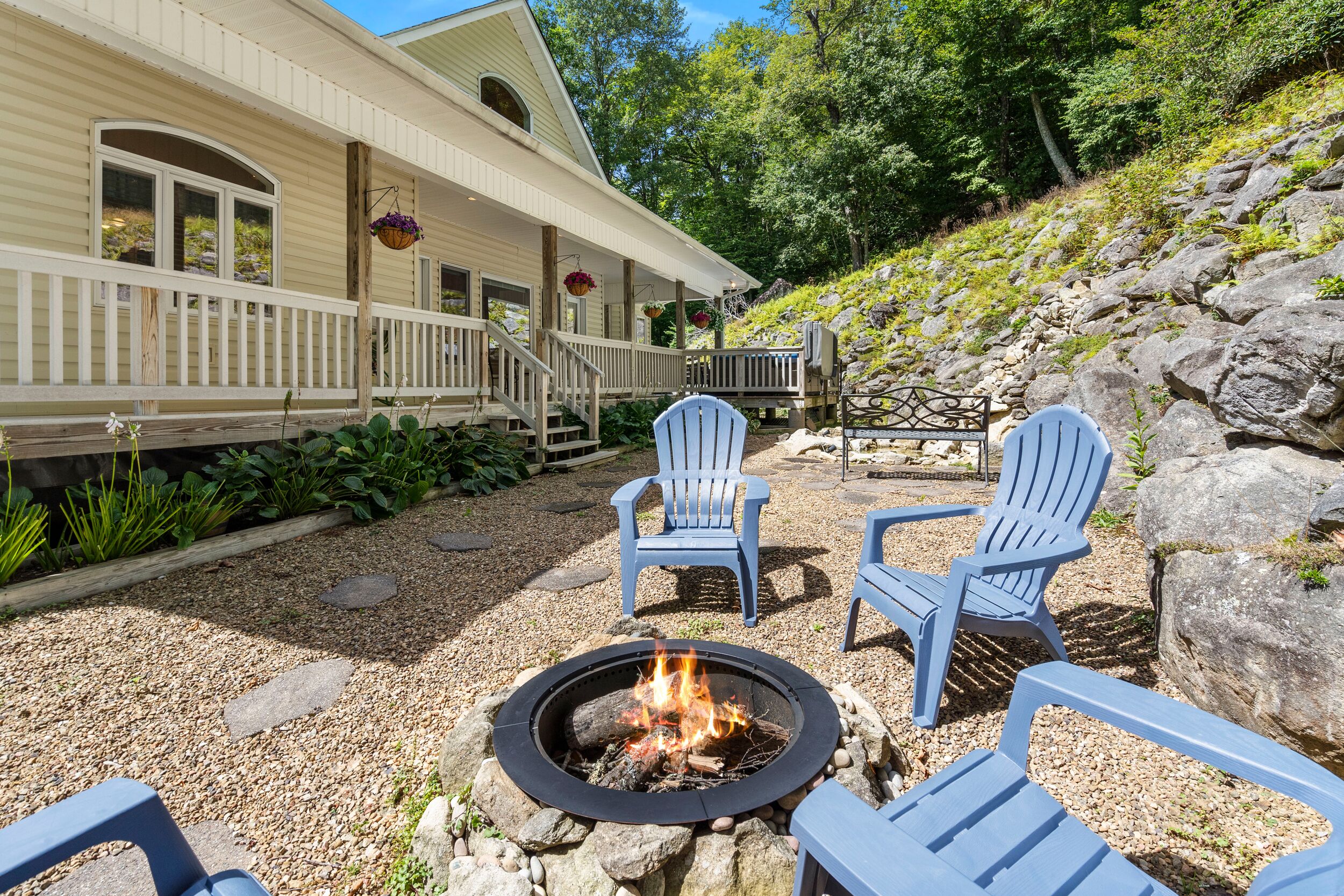 A cozy outdoor seating area with Adirondack chairs, a fire pit, and a stone pathway leading to a building with a porch.