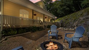A building with a porch, a fire pit, and two Adirondack chairs.
