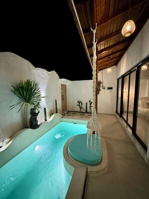 A private pool area with a stone wall, a statue, and a macrame hanging light fixture.