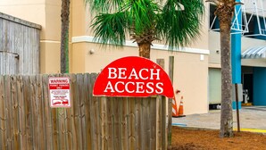 Una valla de madera con un letrero que dice 'Acceso a la playa' y un cartel de advertencia sobre estacionamiento con permiso.