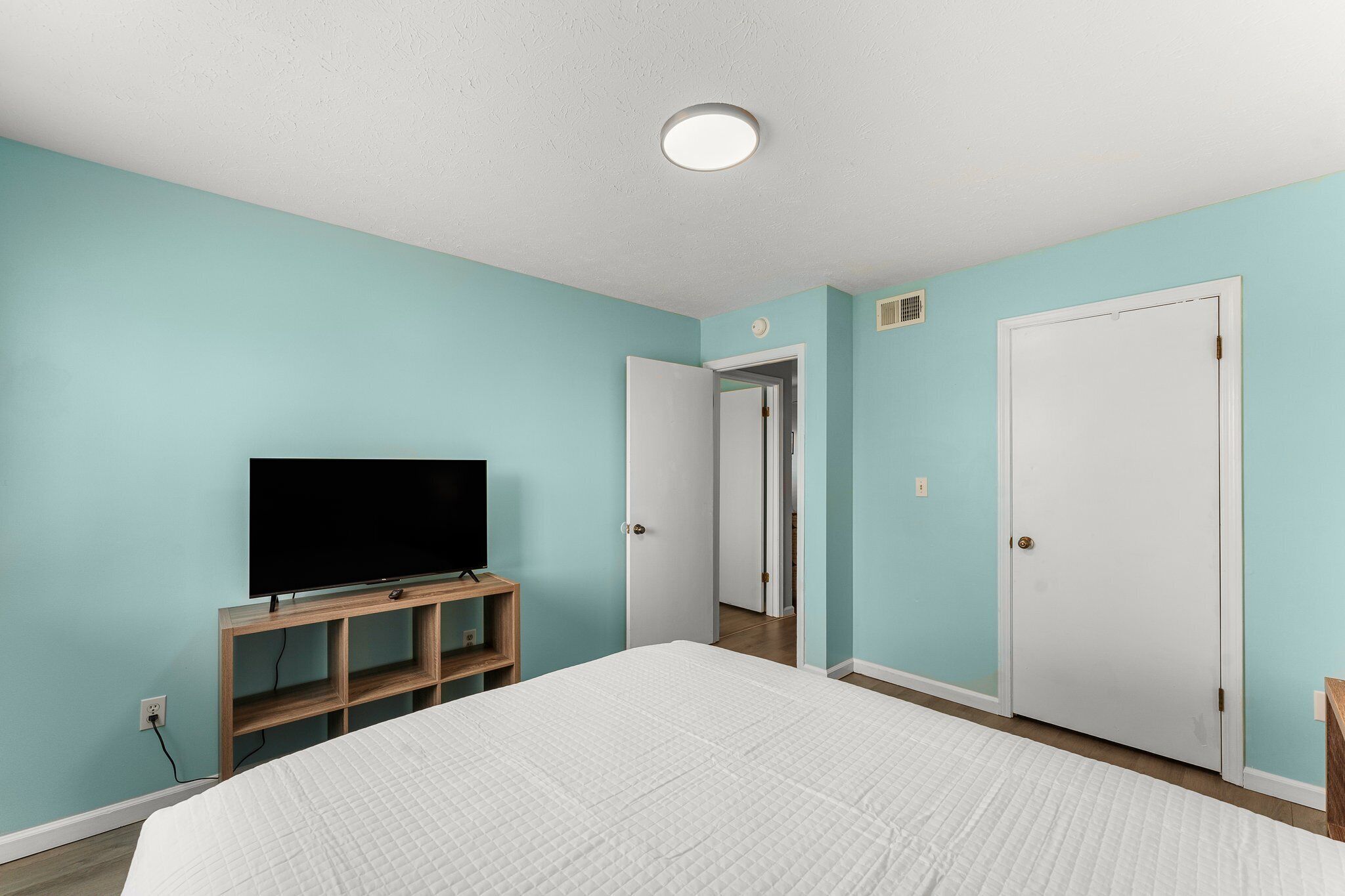 Ein Schlafzimmer mit einem Bett, einem Fernseher auf einem Holzständer und zwei weißen Türen.
