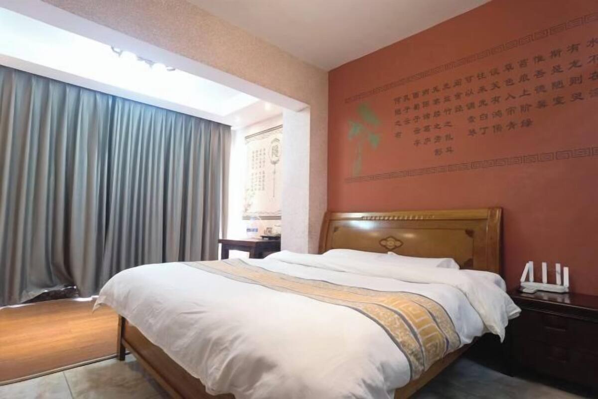 Habitación de hotel con cama, cortinas, mesita de noche y una pared con texto.