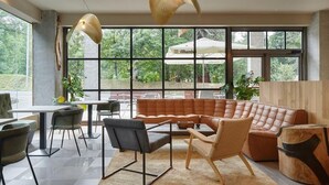 A modern interior with a large window, a brown leather sofa, and a dining area with chairs and a table. - Hotel Sukha (Eskoriatza)