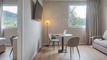 Een moderne woonkamer met een ronde tafel, twee stoelen, een bank en een aan de muur bevestigde televisie.