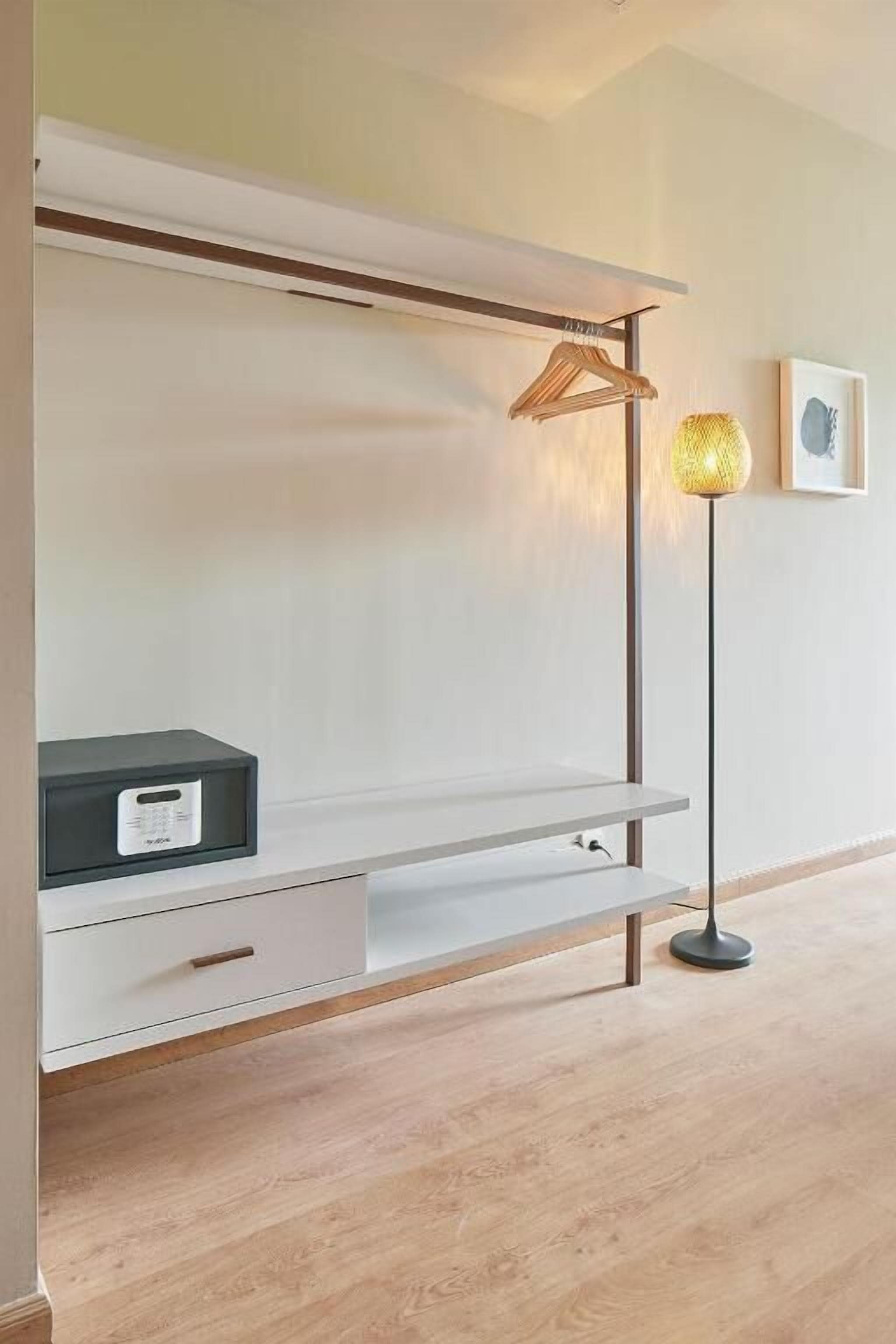 Une pièce au décor minimaliste, avec une console blanche, un lampadaire et un tableau encadré accroché au mur.