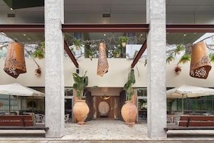 Entrada de hotel con grandes columnas, lámparas colgantes y plantas en macetas.